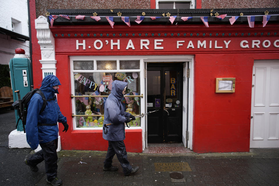 Pedestrians walk along a street in Carlingford, Ireland, Tuesday, April 11, 2023, as final preparations are made for President Joe Biden's visit to the town later in the week. President Biden is visiting Northern Ireland and Ireland to celebrate the 25th Anniversary of the Good Friday Agreement. (AP Photo/Christophe Ena)