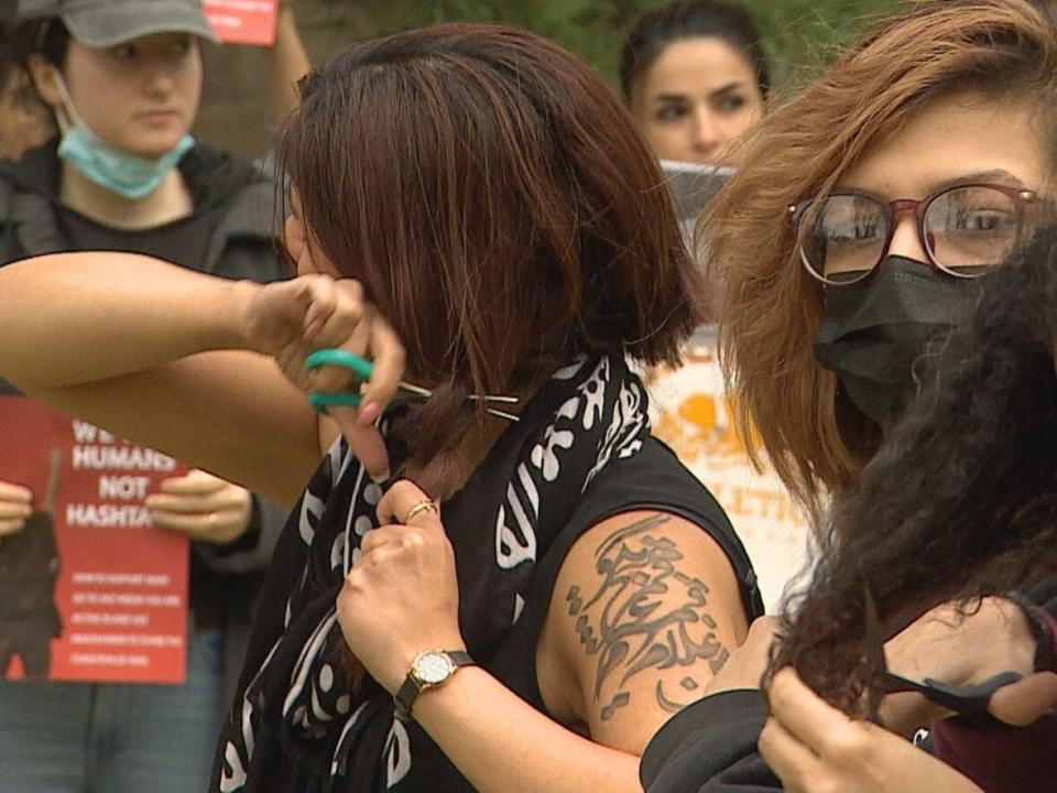 Women cut their hair during a rally in Saskatoon protesting the death of Mahsa Amini. Iran has seen nationwide protests over the death of woman, 22, who was arrested by the morality police for wearing the mandatory Islamic headscarf too loosely and died in custody.  (CBC Saskatchewan - image credit)