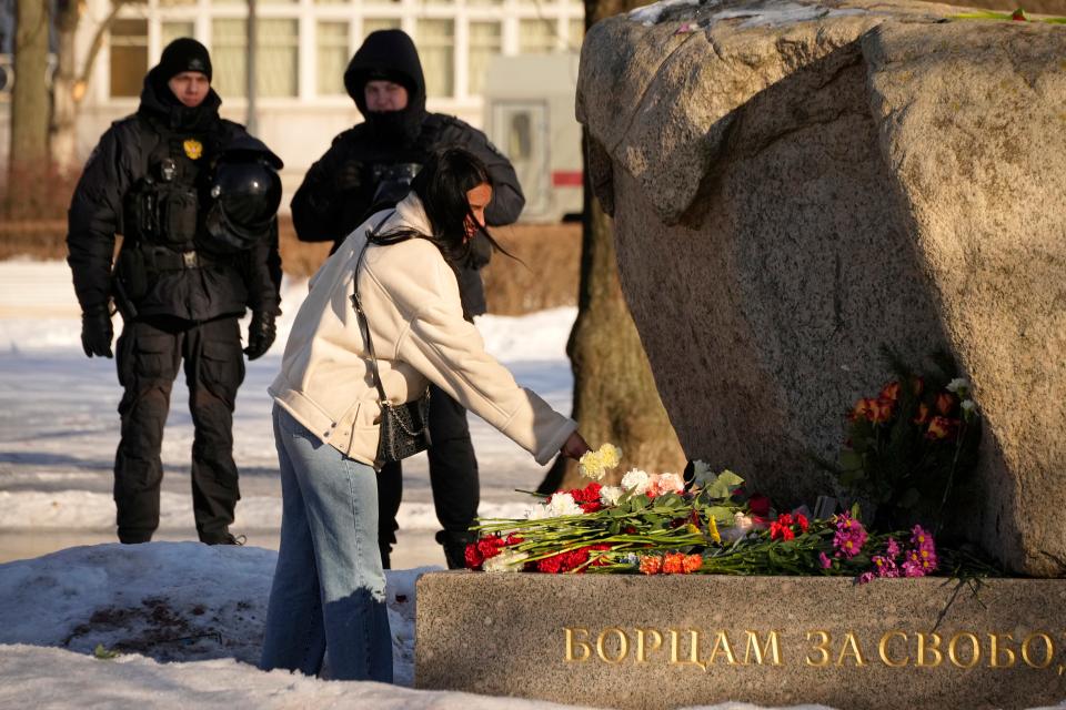 Police officers watch a woman laying flowers to pay tribute to Alexei Navalny in St. Petersburg, Russia, Sunday, Feb. 18, 2024.