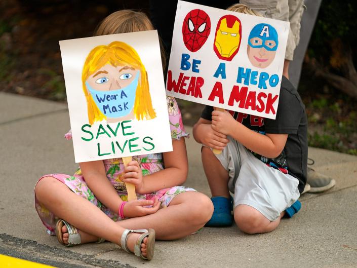 Two kids hold signs encouraging the wearing of masks in the classroom.