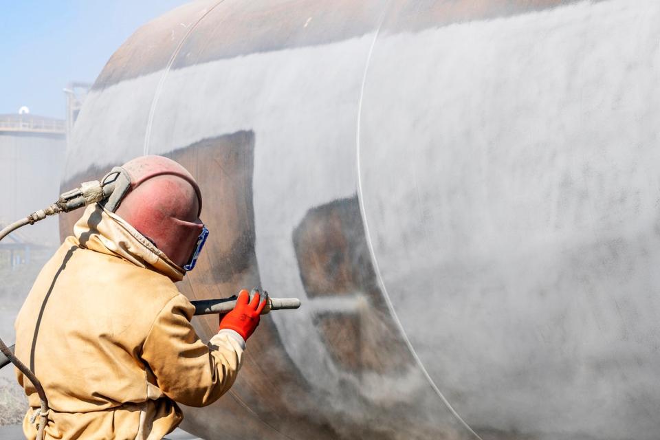 A worker uses a sandblasting tool.