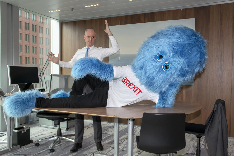 This image made available by the Netherlands Foreign Ministry on Thursday Feb. 14, 2019, shows Foreign Minister Stef Blok and a hairy blue Brexit monster on a desk in The Hague, Netherlands. The Dutch government has enlisted a new ally in its battle to prepare businesses for the impending departure of Britain from the European Union, a hairy blue Brexit monster. A tweet posted Thursday on Foreign Minister Stef Blok's official Twitter feed shows the monster, wearing a white T-shirt emblazoned with the word Brexit in red capital letters, lying across a desk. (Aad Meijer, Netherlands Foreign Ministry via AP)