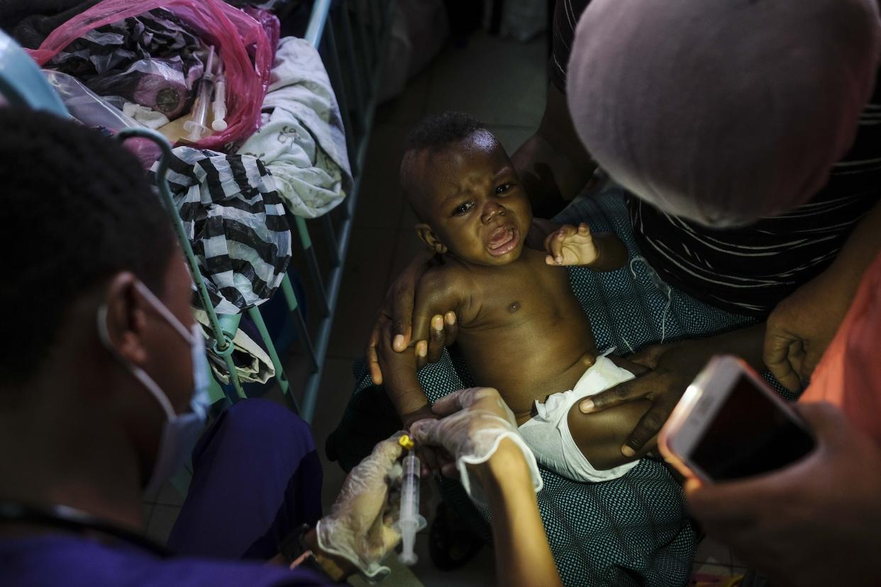 FILE - A healthcare worker places an an intravenous line in the arm of a baby at the La Paix Hospital illuminated with a cellphone flashlight, in Port-au-Prince, Haiti, Oct. 26, 2021. The U.S. government is urging U.S. citizens to leave Haiti given the country’s deepening insecurity and a severe lack of fuel that has affected hospitals, schools and banks. Gas stations remained closed on Thursday, Nov. 11, 2021, a day after the State Department issued its warning. (AP Photo/Matias Delacroix, File)