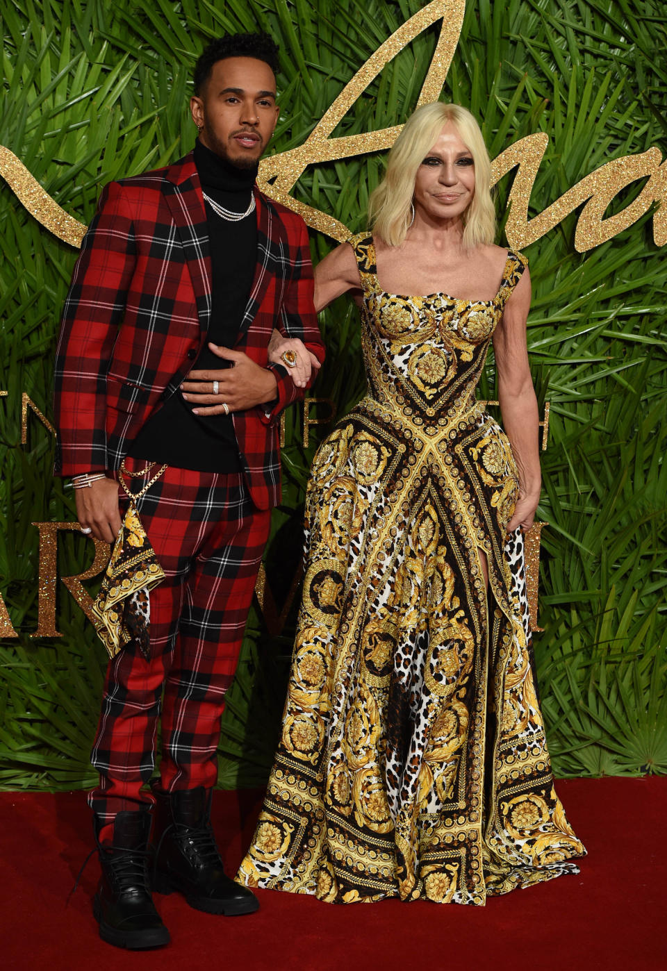 <p>Lewis Hamilton kam in Begleitung von Donatella Versace, die an diesem Abend eine Auszeichnung in der Kategorie „Mode-Ikone“ gewann. Sie trug natürlich ein Kleid ihres eigenen Labels – in dem gleichen opulenten Print-Muster, das auch Musikerin FKA twigs wählte. Lewis Hamilton erschien, wie immer wesentlich mutiger als viele männliche Kollegen, in einem karierten, roten Anzug. Nette Idee: An seiner Hose baumelt ein Einstecktuch, ebenfalls im Versace-Muster des Abends. (Bild: AP Photo) </p>