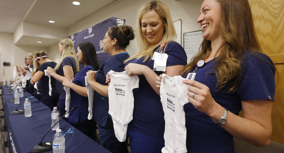 Some of the pregnant nurses who work together hold up baby outfits. Source: AP Photo via AAP