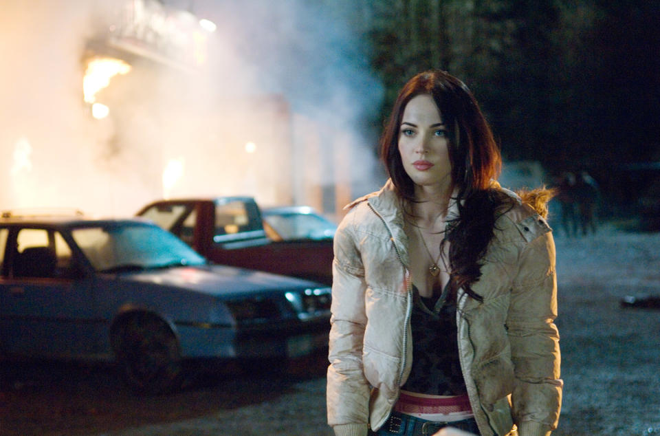 Megan Fox stands in front of a burning building