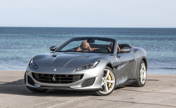 A silver Ferrari Portofino, a convertible, with its top down, parked on a waterfront.