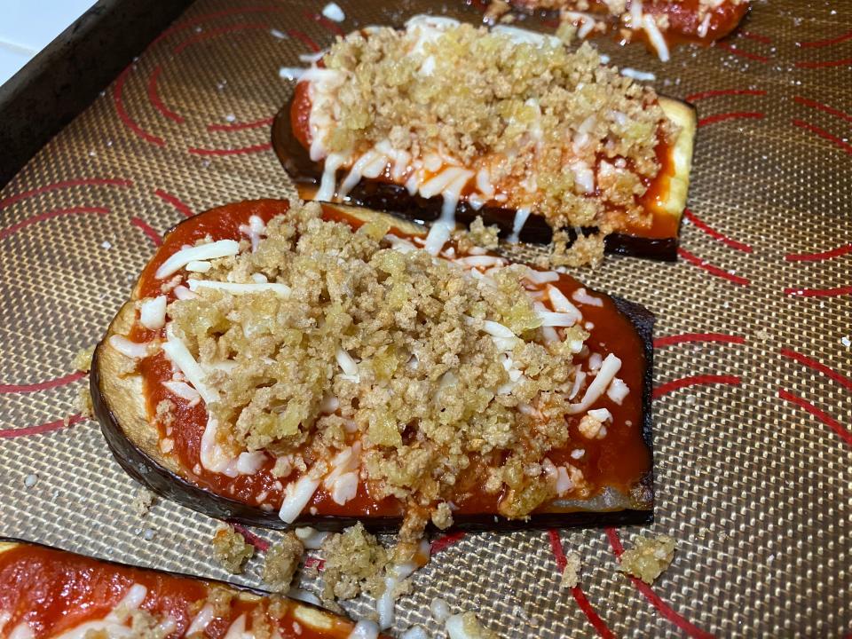 Eggplant slices with marinara sauce, Parmesan, and breadcrumbs on a baking sheet prepared to go in the oven.