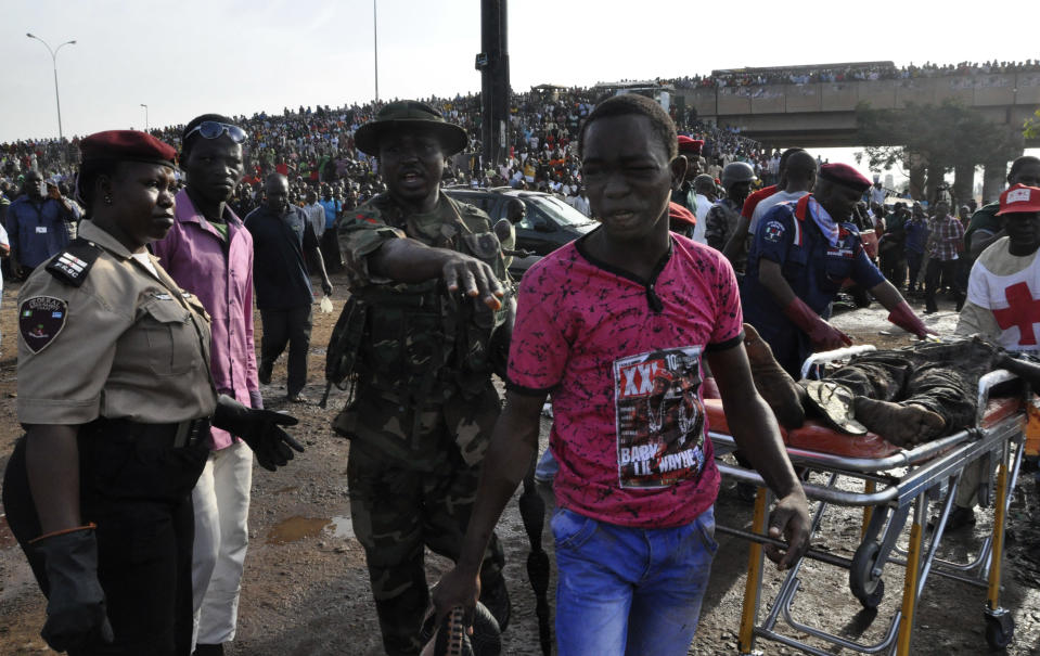 A man is directed by rescue workers as they collect the bodies of victims at the site of a blast at the Nyanya Motor Park, about 16 kilometers (10 miles) from the center of Abuja, Nigeria, Monday, April 14, 2014. An explosion blasted through a busy commuter bus station on the outskirts of Abuja before 7 a.m. (0600 GMT) Monday as hundreds of people were traveling to work. (AP Photo/Gbemiga Olamikan)