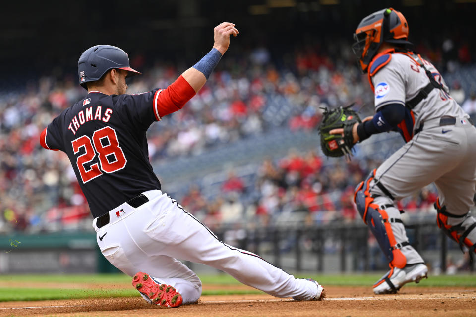 Washington Nationals' Lane Thomas (28) slides into home plate as Houston Astros catcher Victor Caratini, right, waits for the throw on a two-run single by Nationals' Luis García Jr. during the first inning of a baseball game at Nationals Park, Sunday, April 21, 2024, in Washington. (AP Photo/John McDonnell)