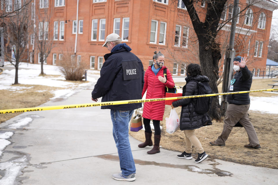 Police officer escorts people past a police line in front of University Hill Elementary School across from the campus of the University of Colorado after a man accused of making mass shooting threats against the college as well as the University of California, Los Angeles, was arrested Tuesday, Feb. 1, 2022, in Boulder, Colo. The police operation caused the evacuation of the elementary school and shelter-in-place orders for nearby residents on Boulder's University Hill. (AP Photo/David Zalubowski)