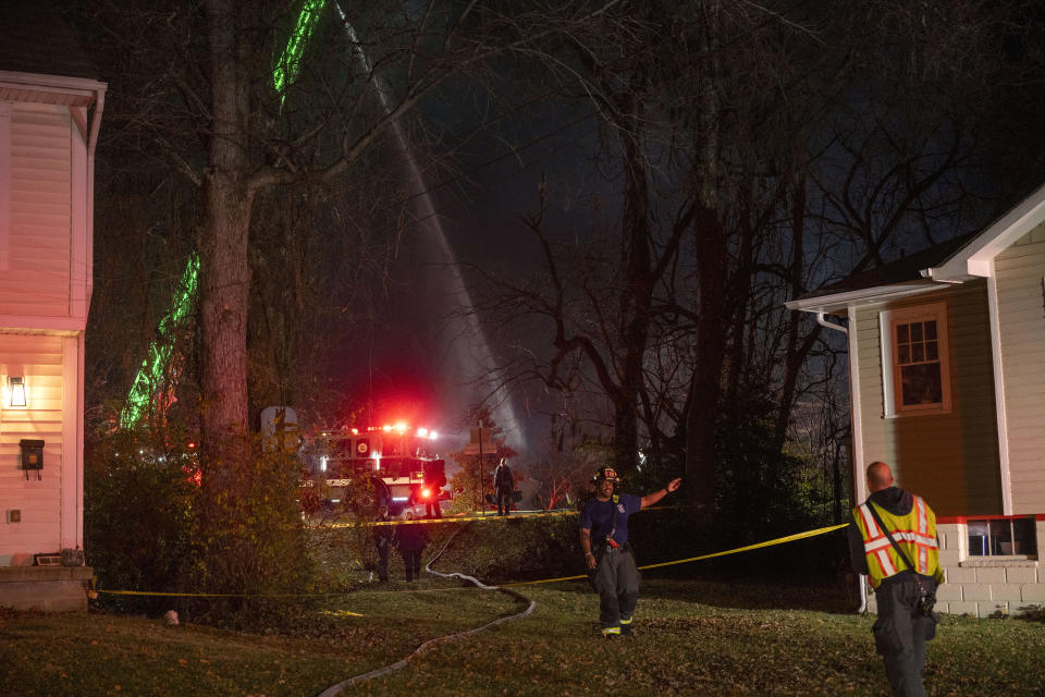 Fire and police officials walk around the scene of a house explosion as an Arlington County Fire Department ladder truck sprays water down on the remains of the building on Monday, Dec. 4, 2023, in Arlington, Va. (AP Photo/Kevin Wolf)