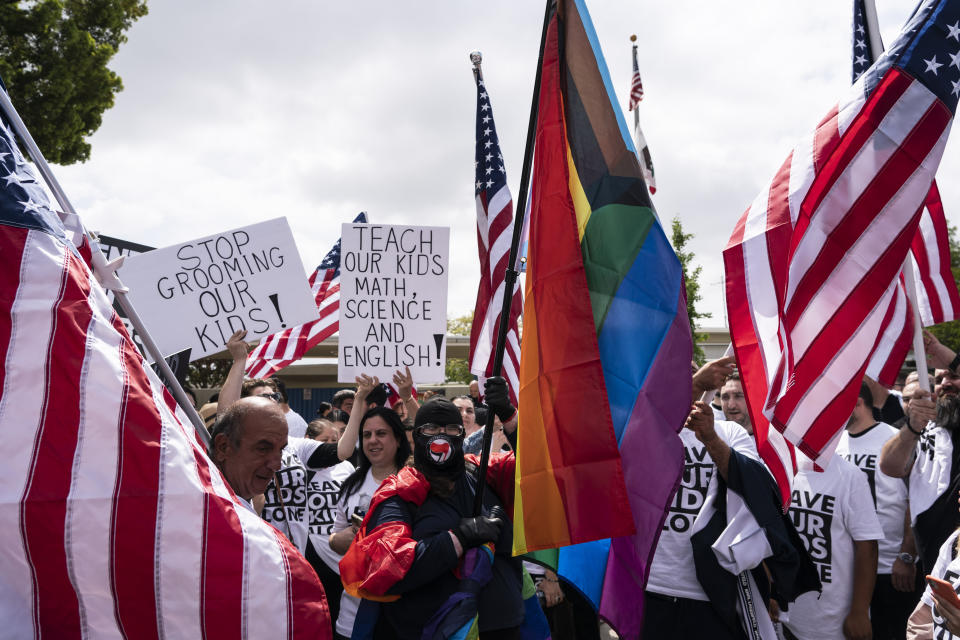 A woman draped in Pride flags is surrounded by people protesting a planned Pride month assembly outside Saticoy Elementary School in Los Angeles, Friday, June 2, 2023. Police officers separated groups of protesters and counter protesters Friday outside the elementary school that has become a flashpoint for Pride month events across California. (AP Photo/Jae C. Hong)