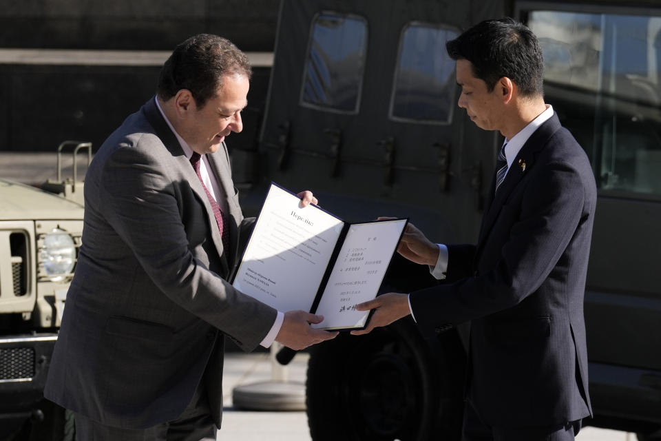 Sergiy Korsunsky, center, Ambassador of Ukraine to Japan, is handed over a document from Toshiro Ino, right, state minister of Defense of Japan, during the handover ceremony of defense equipment for Ukraine at Ministry of Defense Wednesday, May 24, 2023, in Tokyo. the Japan Ground Self-Defense Force's 1/2-ton trucks, seen in background, are part of handover defense equipment. (AP Photo/Eugene Hoshiko)