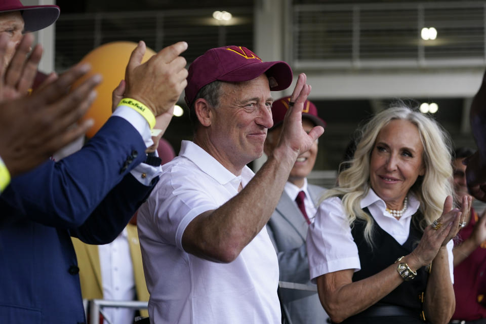 Josh Harris, the leader of a group buying the Washington Commanders, waves to fans at an NFL football pep rally at FedEx Field in Landover, Md., Friday, July 21, 2023. Standing at right is Harris' wife, Marjorie Harris. (AP Photo/Alex Brandon)