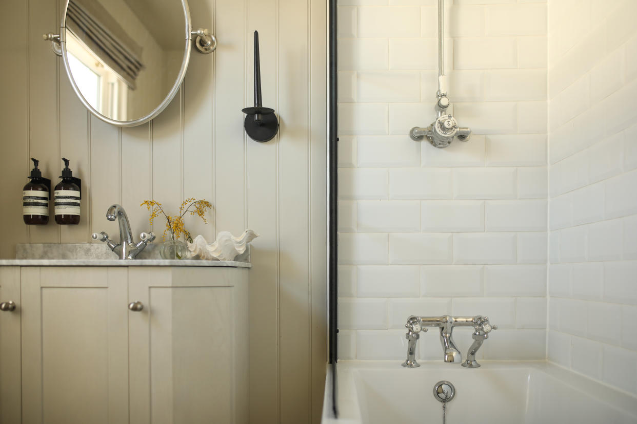  A modern bathroom with cream wood panelled wall, a built-in vanity, and subway tiled bath  