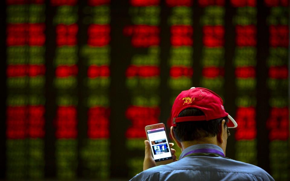 A Chinese investor listens to a news report on his smartphone as he monitors stock prices at a brokerage house in Beijing as US tariffs take effect - AP