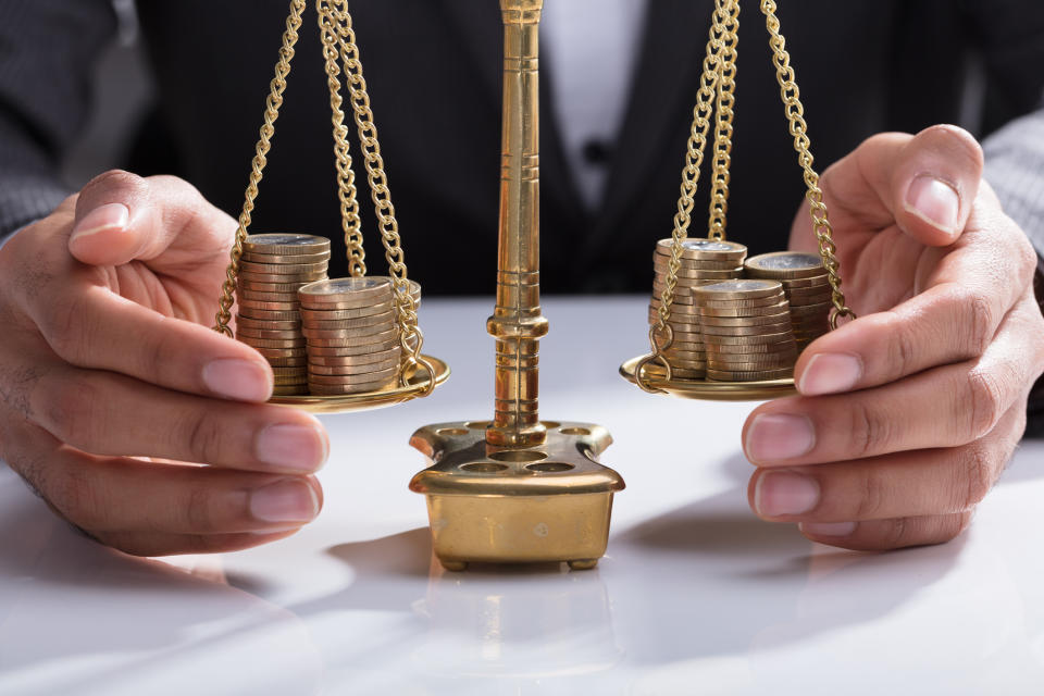 Two hands corral a scale weighing two sets of coins.