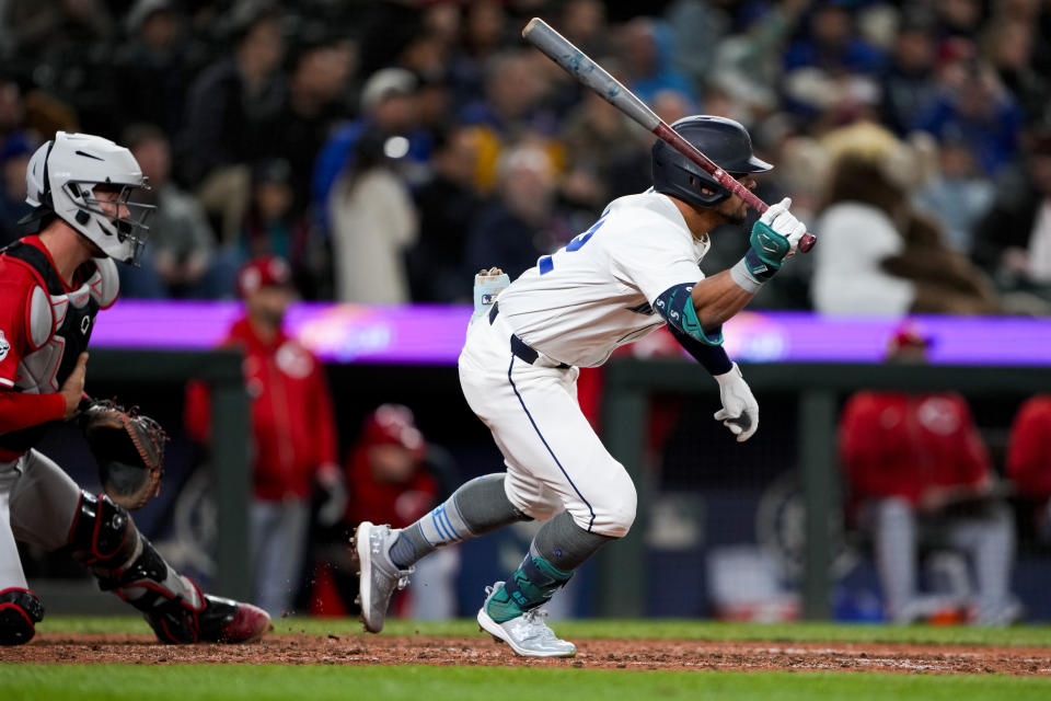 Seattle Mariners' Jonatan Clase follows through on an RBI single for his first major league hit as Cincinnati Reds catcher Tyler Stephenson, left, looks on during the sixth inning of a baseball game Monday, April 15, 2024, in Seattle. (AP Photo/Lindsey Wasson)