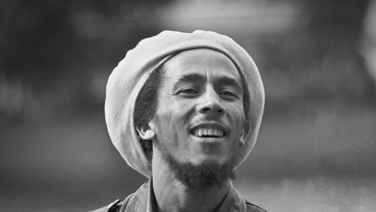 bob marley wearing a leather coat and hat and smiling for a photograph