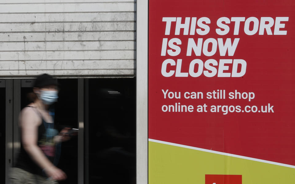 A woman looks at her phone as she walks past a closed branch of a shop in Kensington, London, Wednesday, Aug. 12, 2020. The British economy is on course to record the deepest coronavirus-related slump among the world's seven leading industrial economies after official figures showed it shrinking by a 20.4% in the second quarter of 2020 alone said The Office for National Statistics. (AP Photo/Alastair Grant)