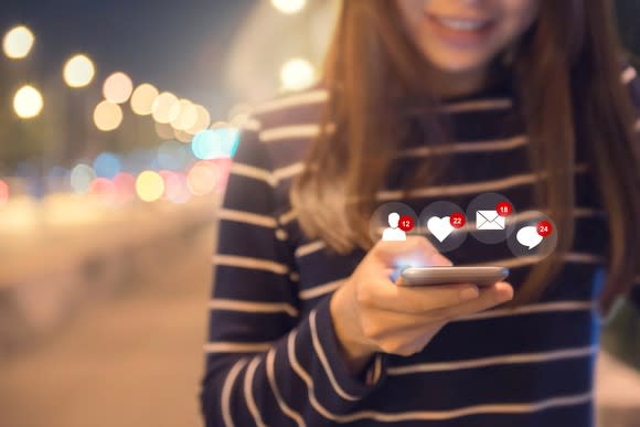 Smiling woman holding a smartphone displaying multiple notifications from social networks