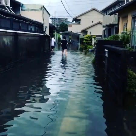 People wade through floodwaters after heavy rains in Mizugae