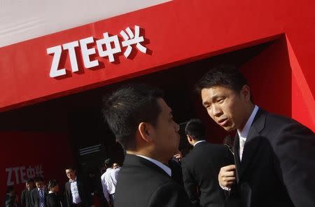 Guests and employees chat under a ZTE company logo in front of the venue of the company's 15th anniversary celebration in Beijing April 18, 2013. REUTERS/Barry Huang