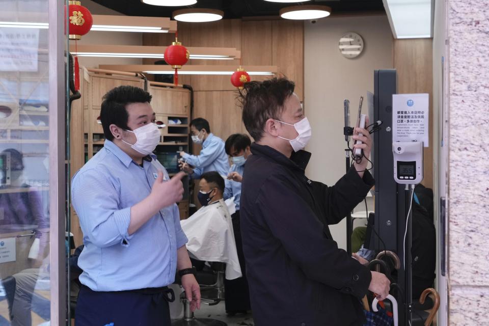 A customer, right, wearing face mask scans QR codes at the entrance before getting haircut at a salon after temporarily closing in Hong Kong, Thursday, March 10, 2022. (AP Photo/Vincent Yu)