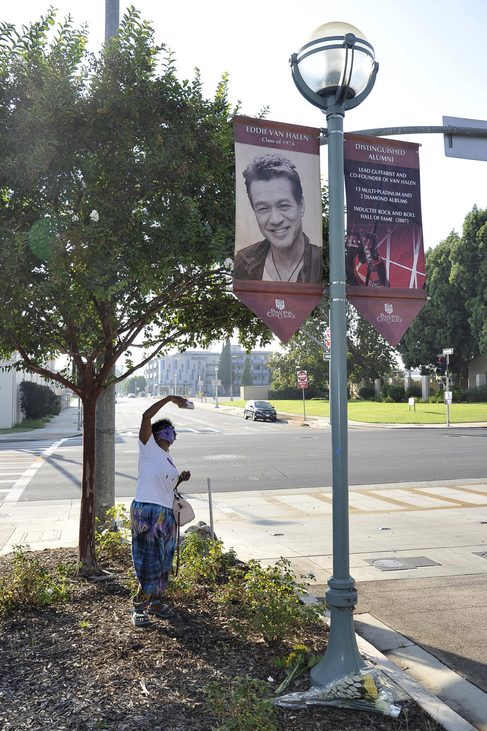 FILE - In this Oct. 6, 2020, file photo Daniel Gaither, of Pasadena, photographs a banner acknowledging distinguished Pasadena City College alumnus Eddie Van Halen at the college in Pasadena, Calif. Van Halen's Southern California hometown will memorialize the late guitar legend, but it's still unclear what form the tribute will take. The Pasadena City Council on Monday, Oct. 26, 2020, directed officials to come up with ideas and report back on how to best remember the rock icon who died of cancer Oct. 6, 2020, at age 65. (Richard Shotwell/Invision/AP, File)