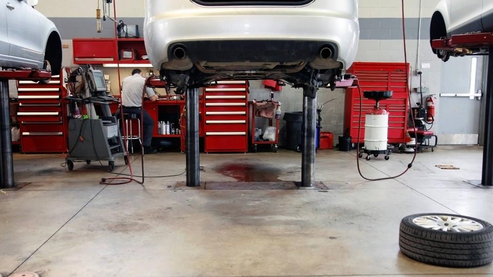 The interior of a car dealership repair facility, shows two cars on hoists.