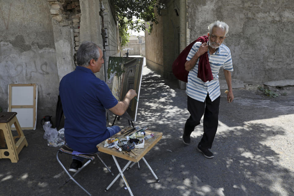 Painter Hassan Naderali paints an old building in the historic neighborhood of Oudlajan, in Tehran, Iran, Monday, June 20, 2022. The overcrowded metropolis may be dusty and in need of beautification, but the old alleyways are nonetheless drawing throngs of artists out of their studios and into the streets. The practice thrived during the pandemic, as artists found solace and inspiration under the open sky when galleries and museums shuttered. (AP Photo/Vahid Salemi)