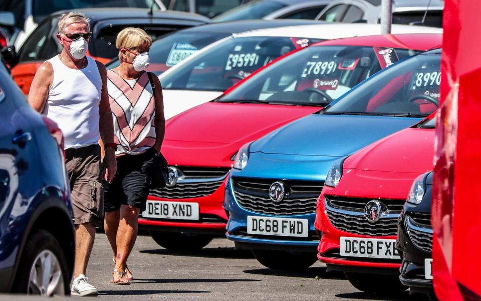 A couple walk past cars on the forecourt of Vauxhall Lookers in Speke, Liverpool - Peter Byrne