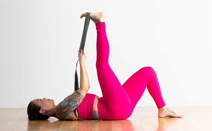 Woman lying on her back with one knee bent and one leg straight and a strap around her lifted leg to stretch her tight hamstrings