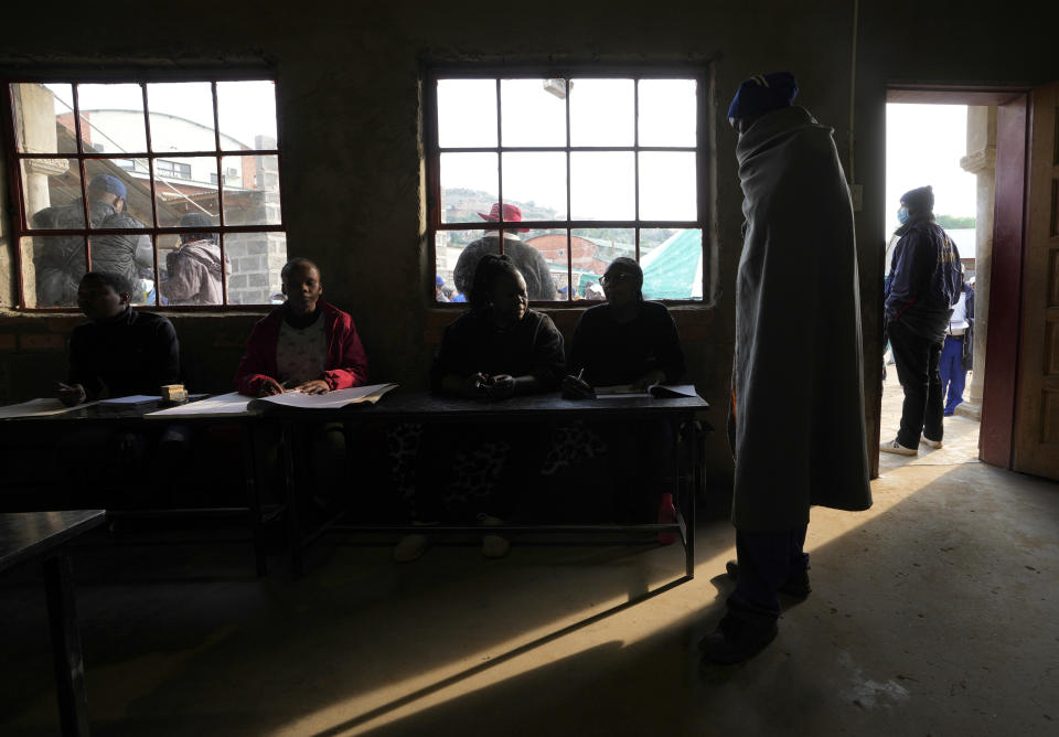 A man wearing a blanket waits as an official checks his name on the electoral register at a poling station in Maseru, Lesotho, Friday, Oct. 7, 2022. Voters across the picturesque mountain kingdom of Lesotho are heading to the polls Friday to elect a leader to find solutions to high unemployment and crime. (AP Photo/Themba Hadebe)