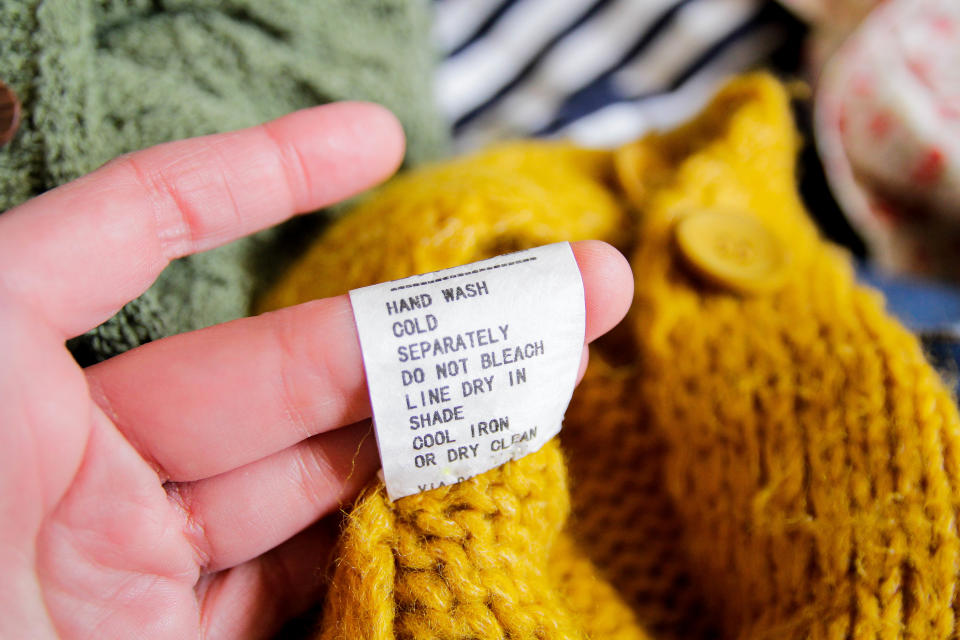 A hand holds up the laundry care instructions on a clothing label