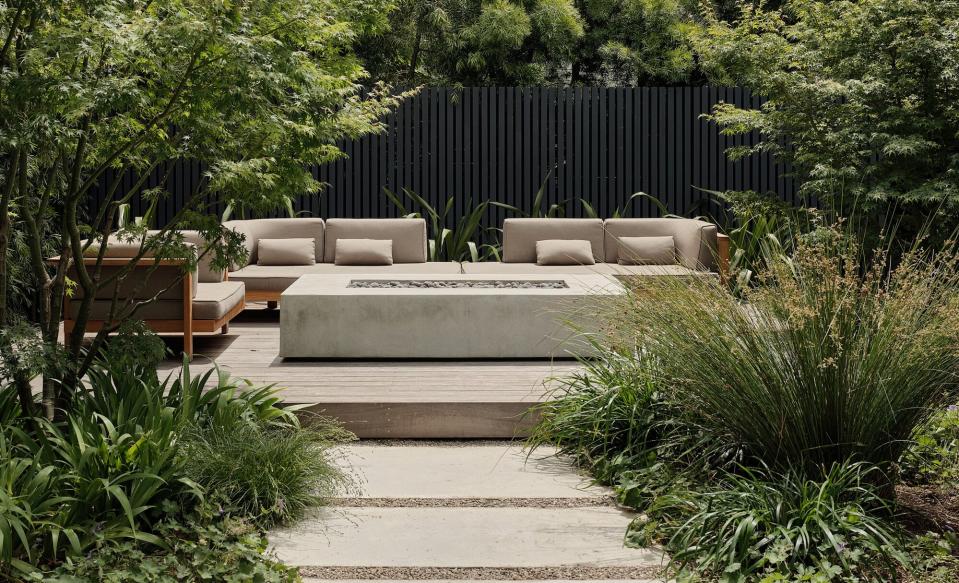 A backyard with concrete firepit and wooden furniture