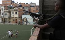 Boys play soccer as a policeman patrols one day after the occupation of the Mare slums complex in Rio de Janeiro, March 31, 2014. The federal troops and police occupied the Mare slums complex on Sunday to help quell a surge in violent crime following attacks by drug traffickers on police posts in three slums on the north side of the city, government officials said. Less than three months before Rio welcomes tens of thousands of foreign soccer fans for the World Cup, the attacks cast new doubts on government efforts to expel gangs from slums using a strong police presence. The city will host the Olympics in 2016. REUTERS/Ricardo Moraes (BRAZIL - Tags: CRIME LAW SPORT SOCCER WORLD CUP SOCIETY)