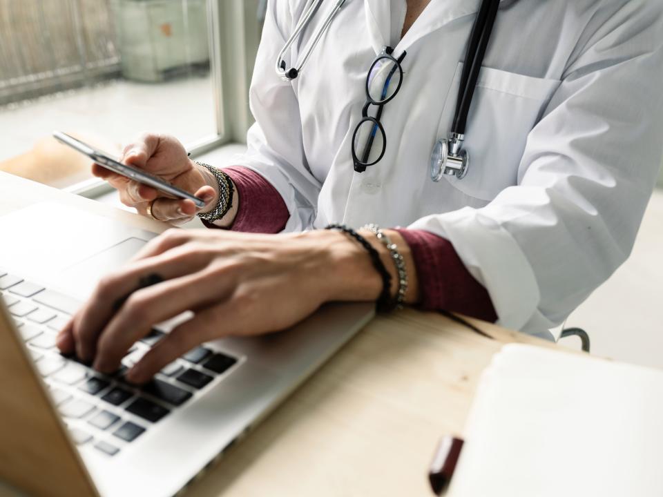 Doctor uses computer an smartphone simultaneously.