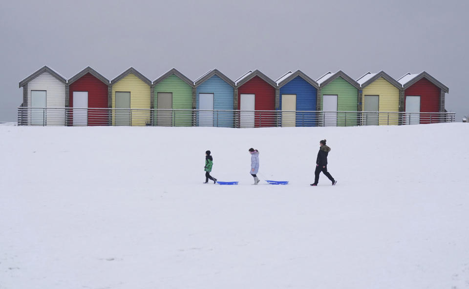 People walk through the snow beside the beach huts at Blyth in Northumberland, England, Sunday, Dec. 3, 2023 as temperatures are tipped to plunge to as low as minus 11C (12.2 F) in parts of the UK over the weekend. (Owen Humphreys/PA via AP)