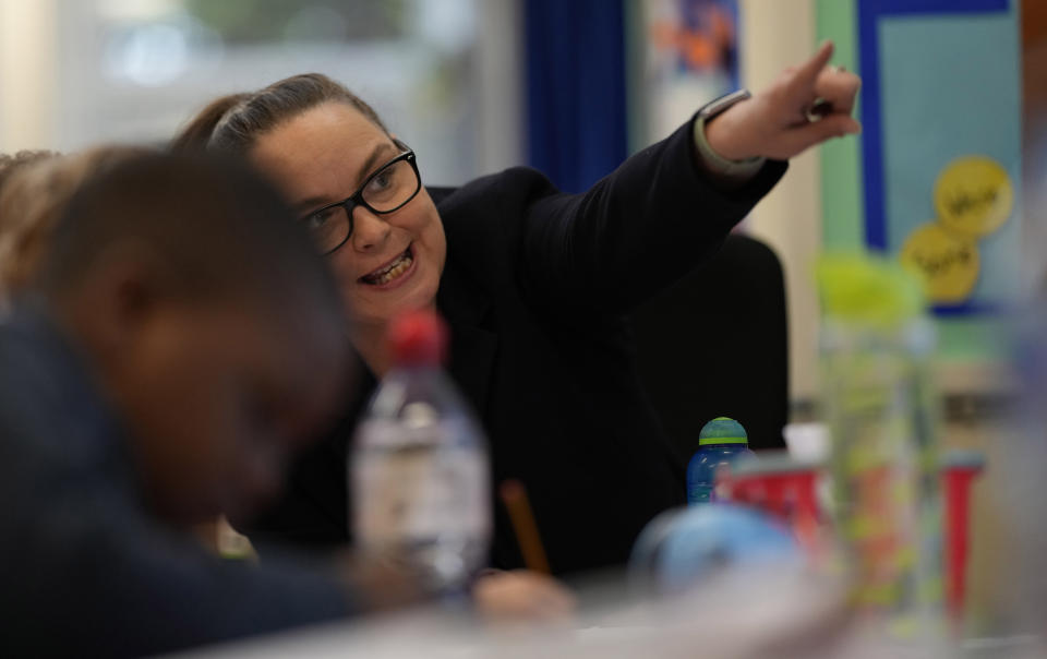 Colette Doran-Hannon the Executive Principal of the Holy Family Catholic Primary School gestures towards the information display as she helps pupils in a year 1 writing class at the school in Greenwich, London, Wednesday, May 19, 2021. Before anyone had ever heard of COVID-19, Doran-Hannon was dispatched to the school to get it back on track after years of poor management that had left it with 10 pounds in the bank and eight laptops for more than 160 students. (AP Photo/Alastair Grant)
