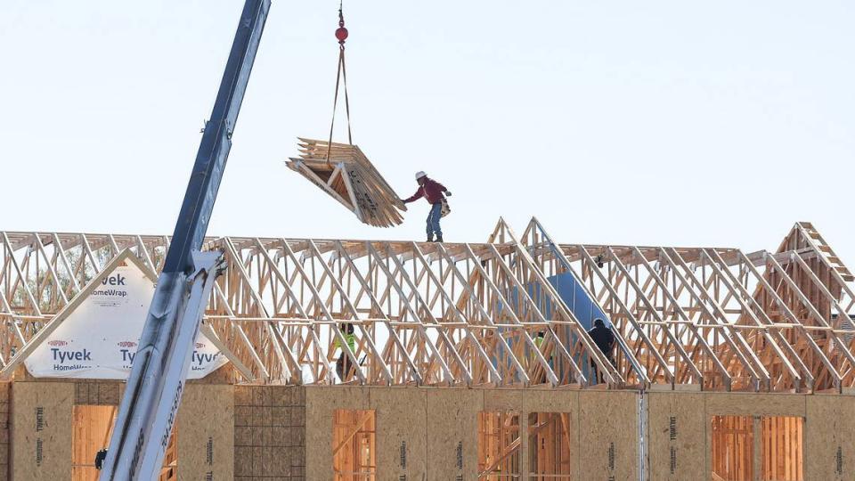 Perched atop the roof of townhomes under construction near Charlotte’s University City neighborhood, a worker reaches for a load of trusses from a crane. The worker is not tethered to the roof, so there is nothing to stop him from falling.