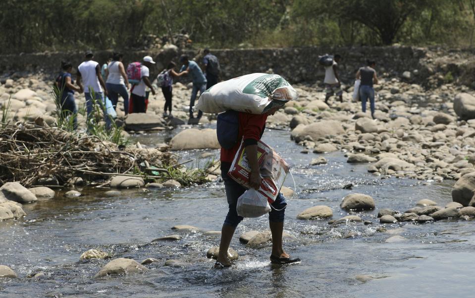 Venezuelans cross the Tachira River with supplies they bought in Colombia as they trek back to Venezuela near the Simon Bolivar International Bridge in La Parada, Colombia, Monday, Feb. 25, 2019. Venezuela continues to keep its borders closed to keep humanitarian aid from entering. (AP Photo/Fernando Vergara)