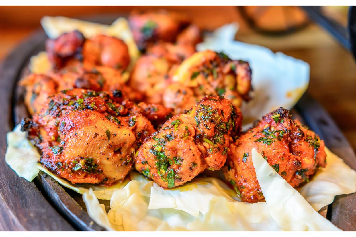 Closeup of tandoori chicken on an iron skillet surrounded by a wood underliner with a blurred background