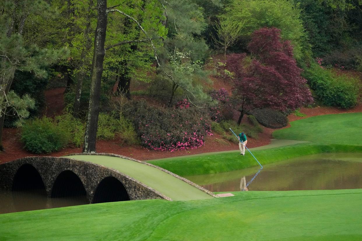 Apr 6, 2022; Augusta, Georgia, USA; A course worker cleans debris from Rae's Creek next to the Ben Hogan Bridge on no. 12 during a practice round of The Masters golf tournament at Augusta National Golf Club. Mandatory Credit: Rob Schumacher-USA TODAY Sports