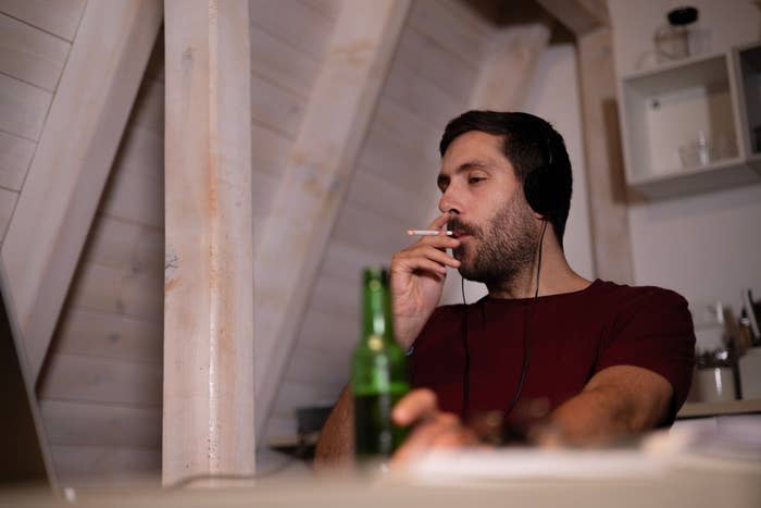 a man drinking a beer and smoking a cigarette