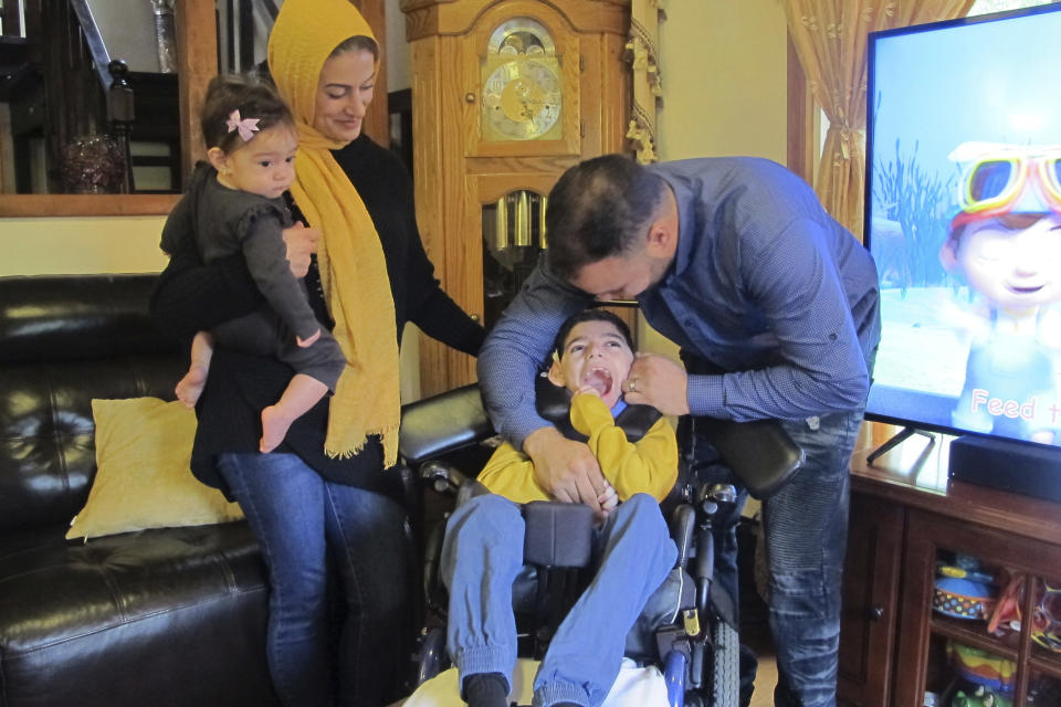 In this Monday, Oct. 7, 2019 photo, Ali Hamideh plays with his 9-year-old son, Ameer, inside the family's home in Blasdell, NY, as Ameer's mother, Ooroba Hamideh, holding daughter Aya Hamideh, looks on. The Hamidehs say Ameer was unfairly removed from school after the district rejected his medical exemption for vaccines. New York has tightened the criteria for medical exemptions after doing away altogether with religious exemptions. (AP Photo/Carolyn Thompson)