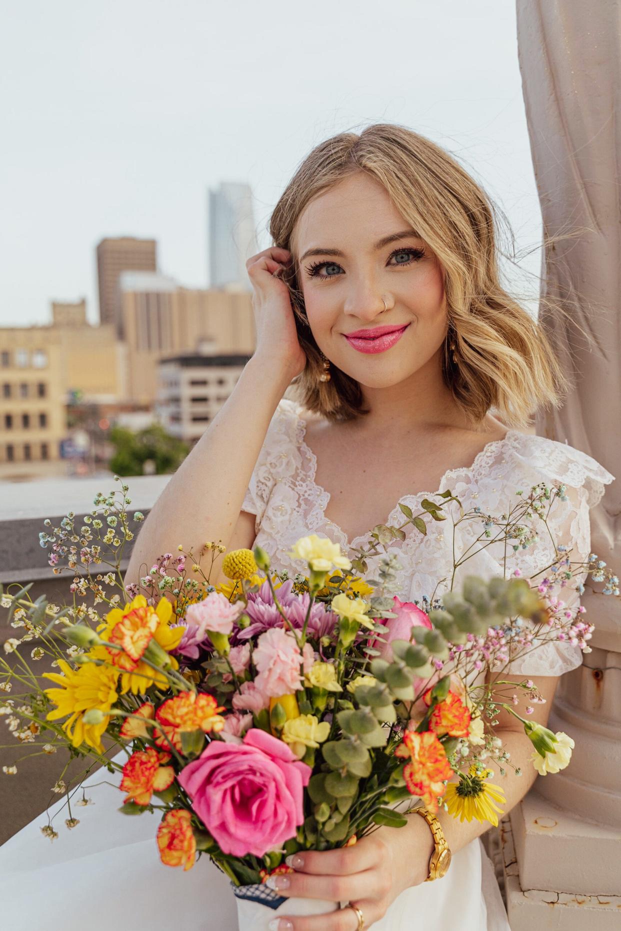 A bride tucks her hair behind her ear as she holds a bouquet of flowers.