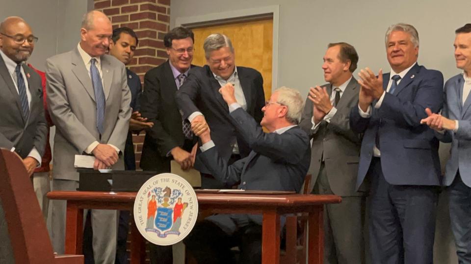 New Jersey Gov. Phil Murphy, sitting, shakes hands with Netflix Co-CEO Ted Sarandos after handing him the ceremonial pen he used to sign a document that begins the review period on an amendment to Fort Monmouth's reuse plan, allowing for film and television production campus at the former Army post.