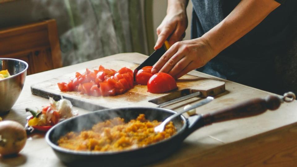 Una persona picando un tomate en una tabla de madera